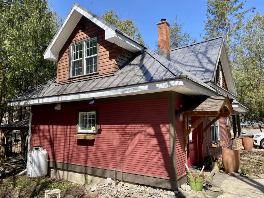 Muskoka cottage with red siding, gabled roof, and surrounding trees, perfect for a relaxing getaway.