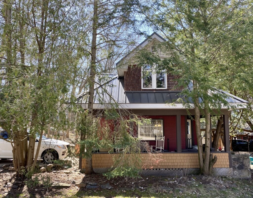 Charming Muskoka cottage surrounded by trees with a front porch and parked cars.