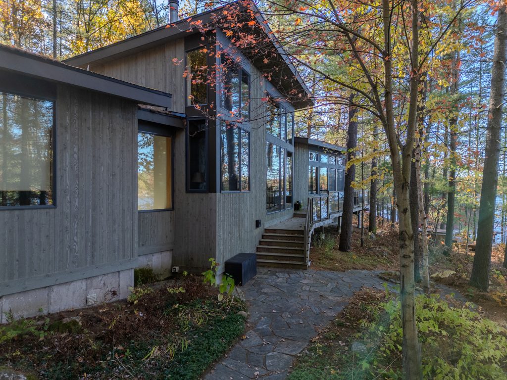 Contemporary Muskoka cottage with large windows and a stone path through the fall forest.