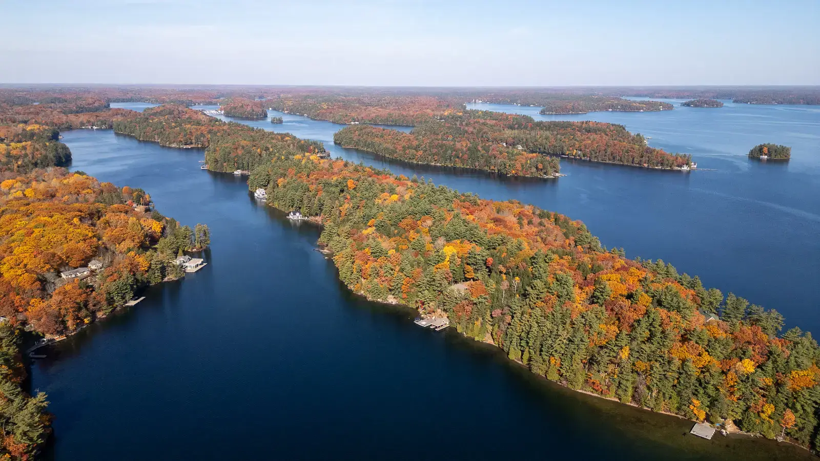 Wide-angle aerial drone view of Lake Joseph, Muskoka, showcasing numerous islands and forested shorelines with vibrant fall colors surrounding deep blue water.