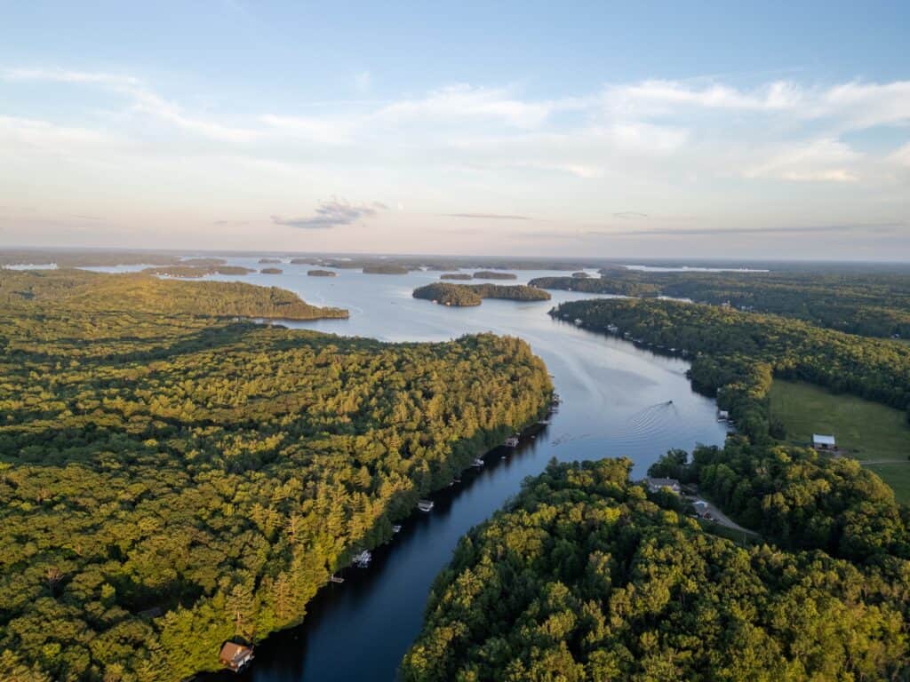 Aerial view of Lake Muskoka, a narrow channel opening into island-dotted open water at golden hour